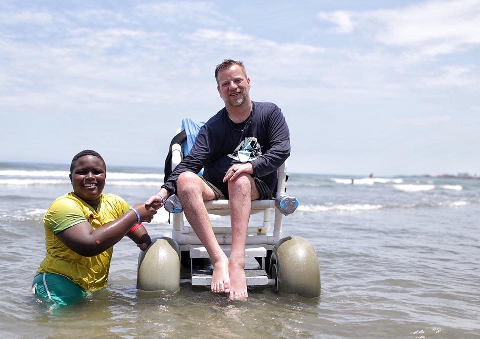 young man in water shaking hands with man in beach wheelchair