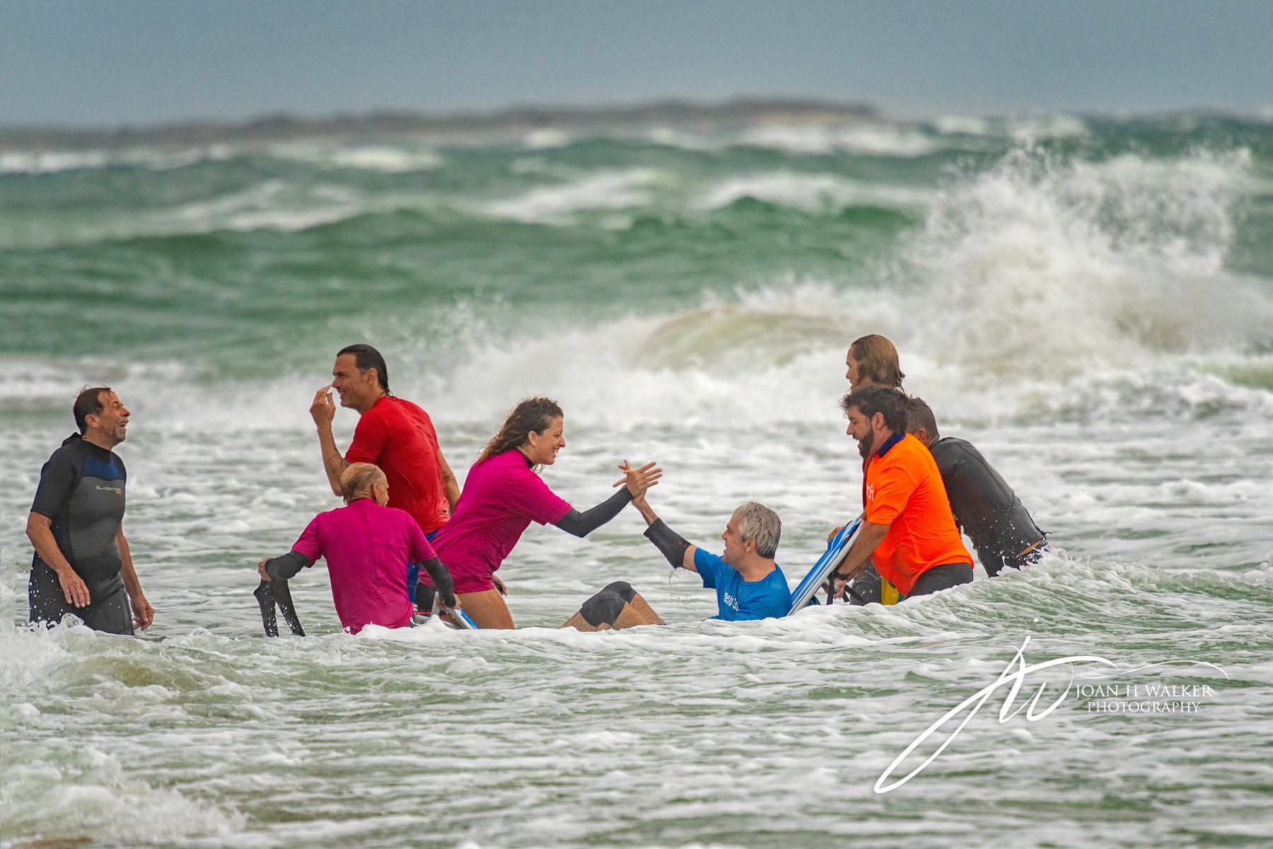 adaptive surfer and volunteer giving high fives in front of big waves