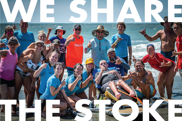 adaptive surfer on seated board with group of volunteers giving thumps up