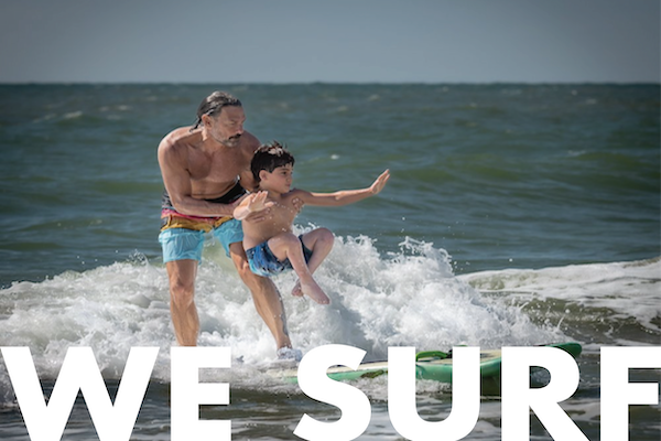 surfer holding boy with legs crossed on surfboard