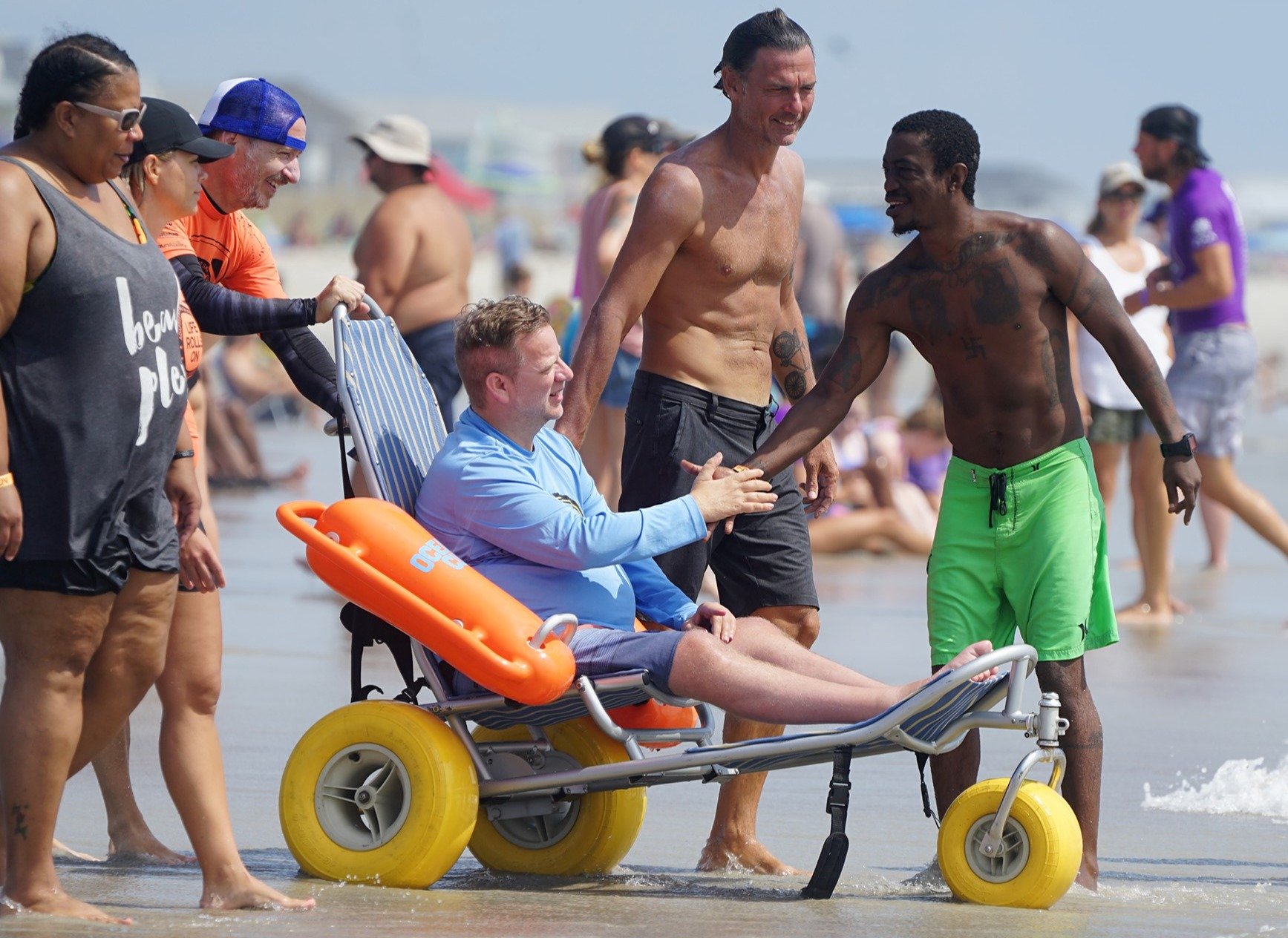 man in beach wheelchair shaking hands with volunteer